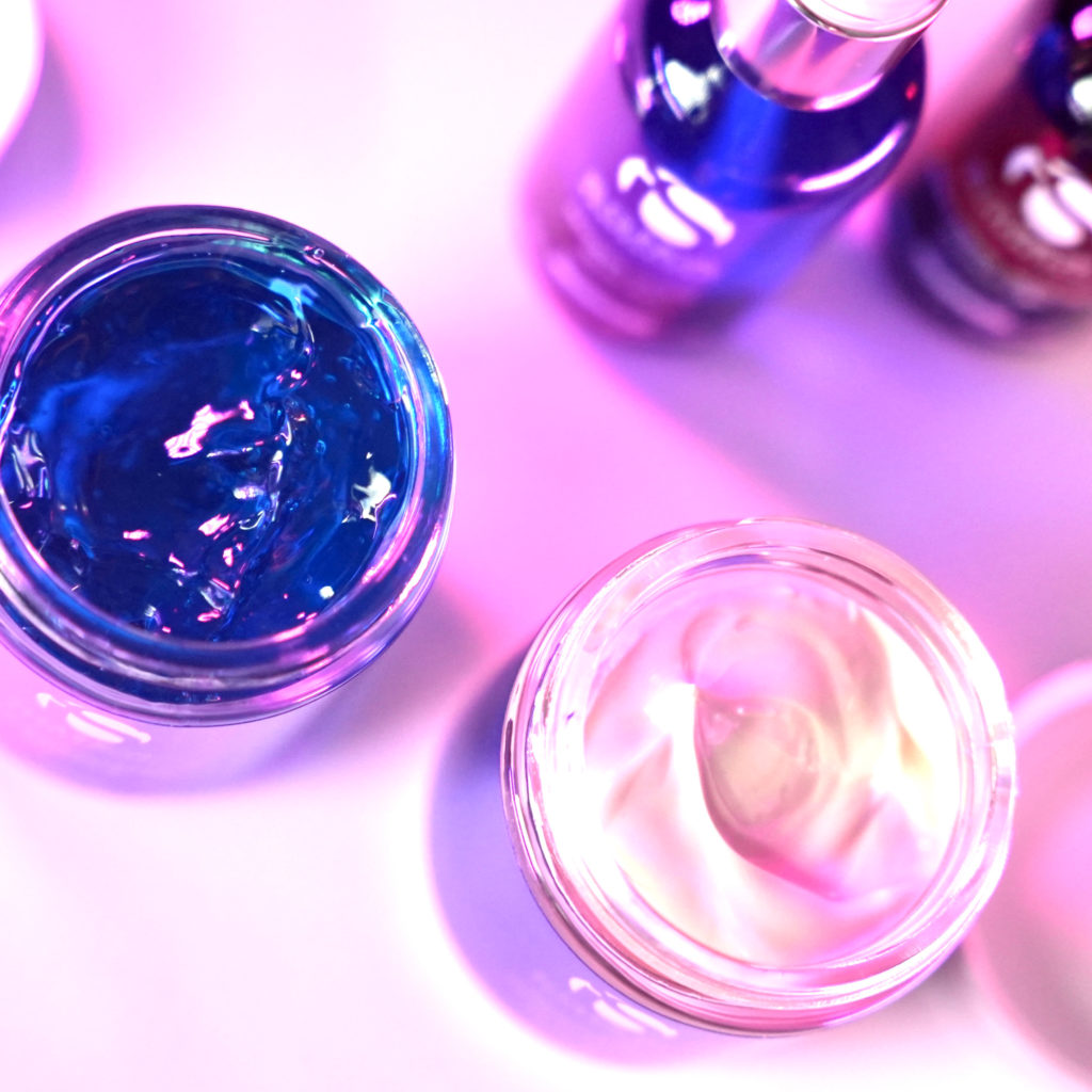 A closeup photo of facial products in a purple gradient backdrop.